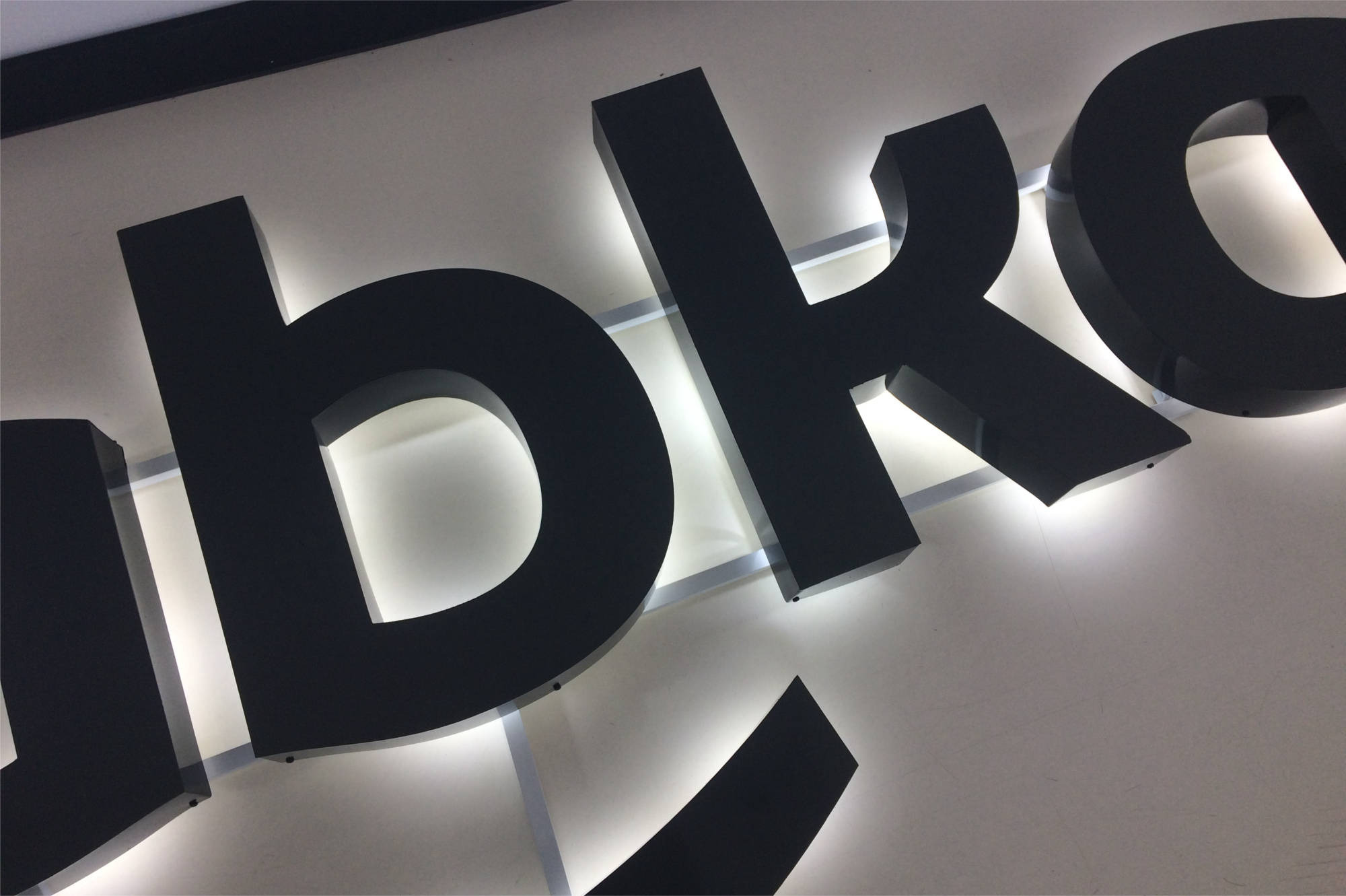 Czarne, przestrzenne litery z podświetleniem na jasnej ścianie, tworzące napis 'abko', widoczne z dołu pod kątem.