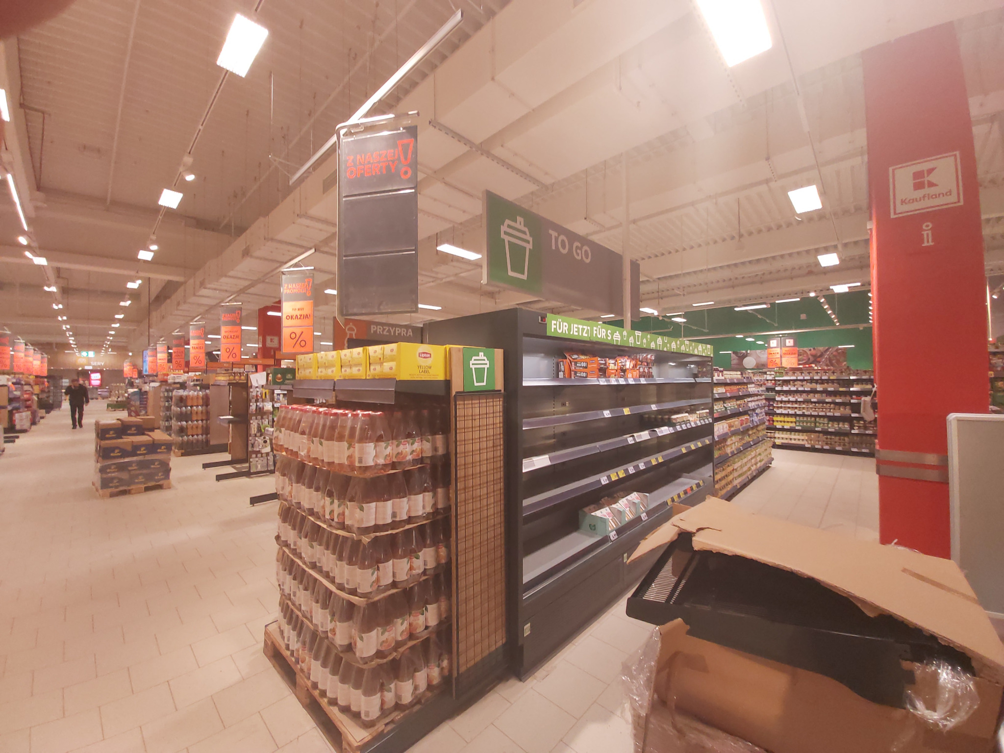 Zdjęcie wnętrza sklepu Kaufland w Luboniu z pustymi półkami w dziale 'To Go' i stertami napojów na paletach, z widocznym znakiem 'Z Naszej Oferty'.