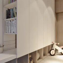 Pokój dziecięcy z białymi szafami w zabudowie, regałem z książkami, biurkiem z przyborami do pisania i drewnianym rowerkiem biegowym.