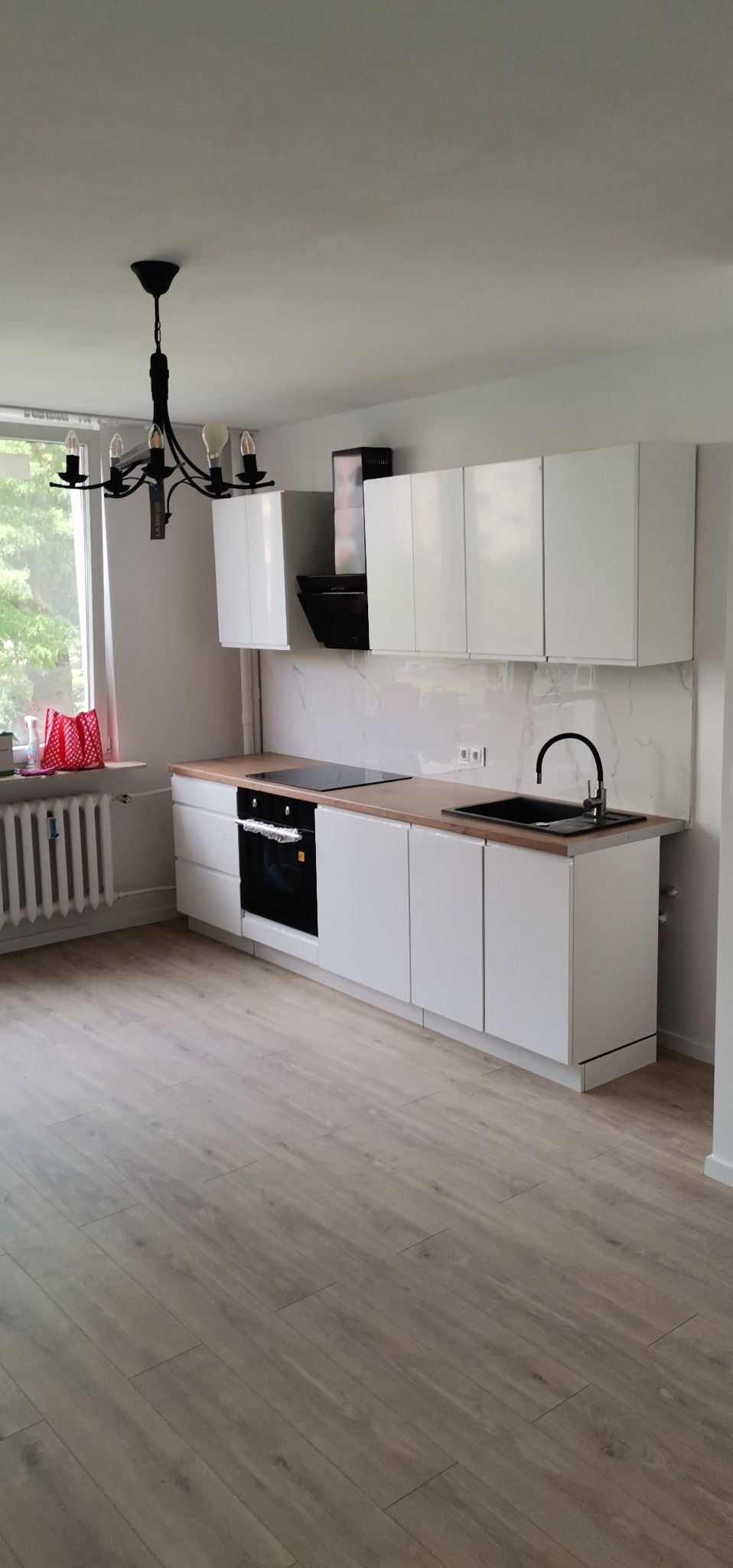 Nowoczesna kuchnia z białymi szafkami, drewnianym blatem, czarną armaturą i marmurową ścianą nad blatem, widziana z perspektywy podłogi z paneli.