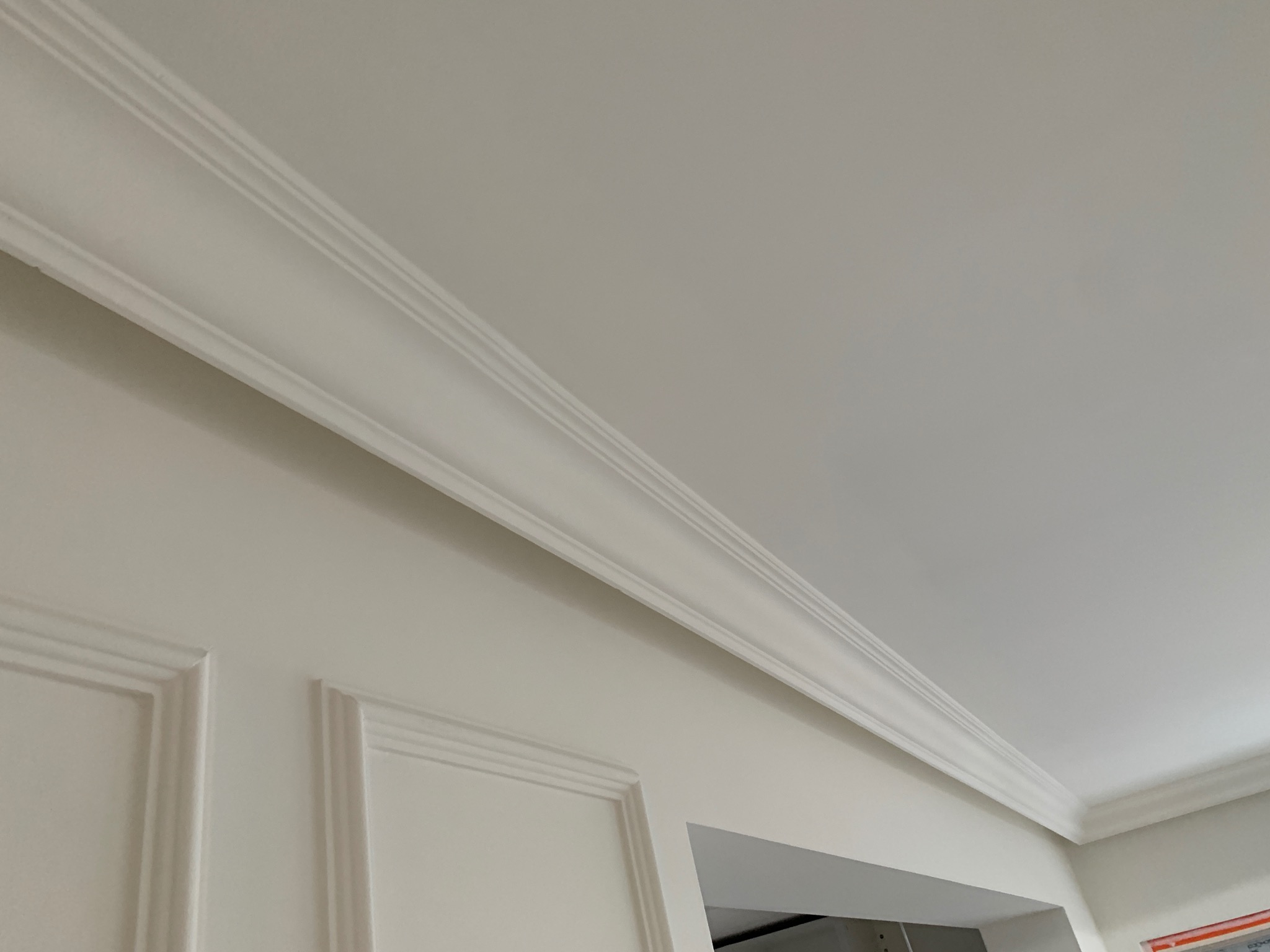 Białe, ozdobne listwy przypodłogowe i sufitowe, zamontowane w rogu pokoju, widoczne pod kątem od dołu.