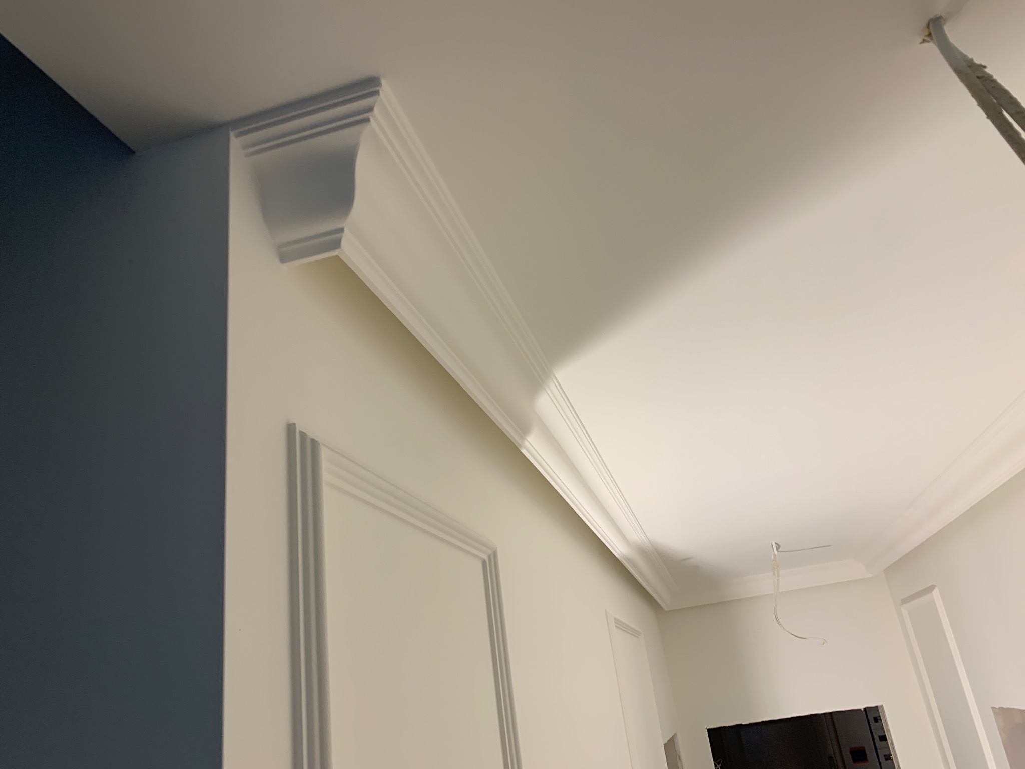 Wnętrze z zamontowaną sztukaterią sufitową i ścienną, widoczne przewody wystające z sufitu, ściana pomalowana częściowo na granatowo.