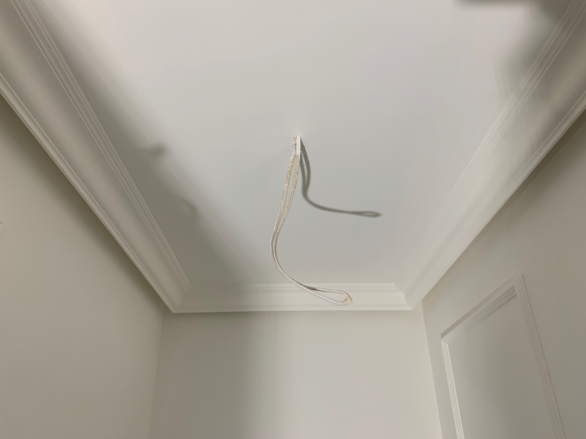 Białe wnętrze w trakcie prac wykończeniowych, widoczne przewody wystające z sufitu z ozdobnymi listwami.