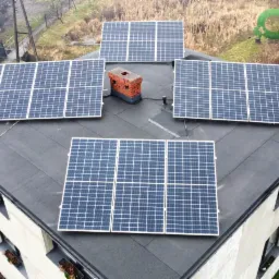 Instalacja fotowoltaiczna na dachu domu jednorodzinnego z kominem z cegły, widok z góry, panele ułożone w kilku rzędach.