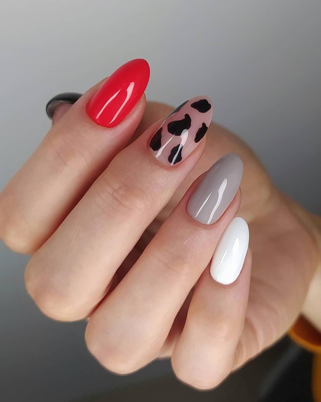 Dłoń z pomalowanymi paznokciami w kolorach: czerwonym, szarym, białym oraz z wzorem w czarne cętki na beżowym tle.