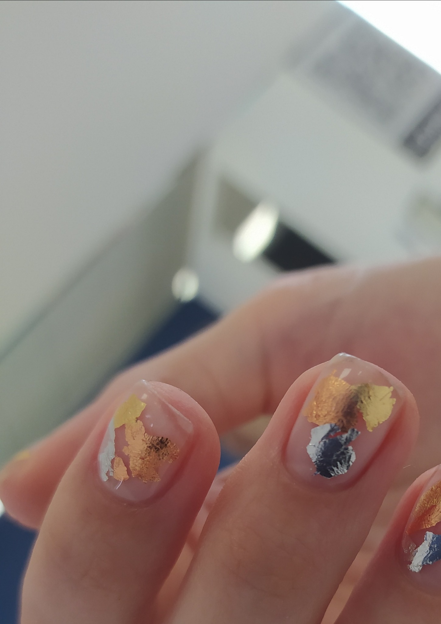 Delikatny, transparentny lakier z aplikacją złotych i srebrnych płatków na paznokciach