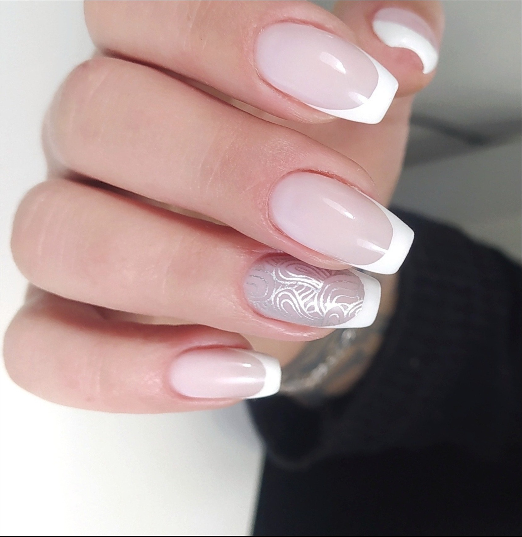 Dłoń z perfekcyjnie wykonanym french manicure, jeden paznokieć zdobiony delikatnym, srebrnym wzorem.