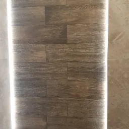 Panel ścienny imitujący drewno z oświetleniem LED po bokach i metalowym uchwytem na ręczniki w kształcie litery U.