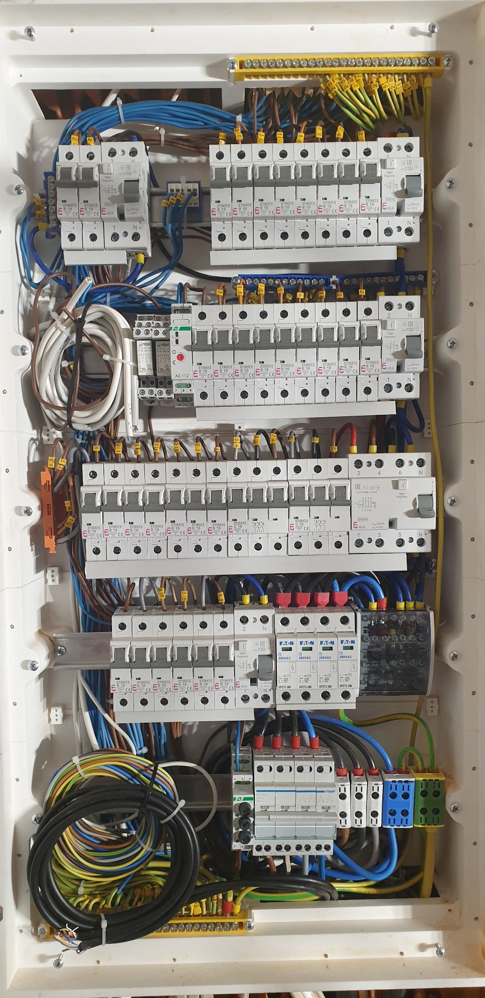 Rozdzielnica elektryczna z licznymi bezpiecznikami, okablowaniem w kolorach niebieskim, żółto-zielonym i brązowym, widoczne elementy montażowe i złącza.