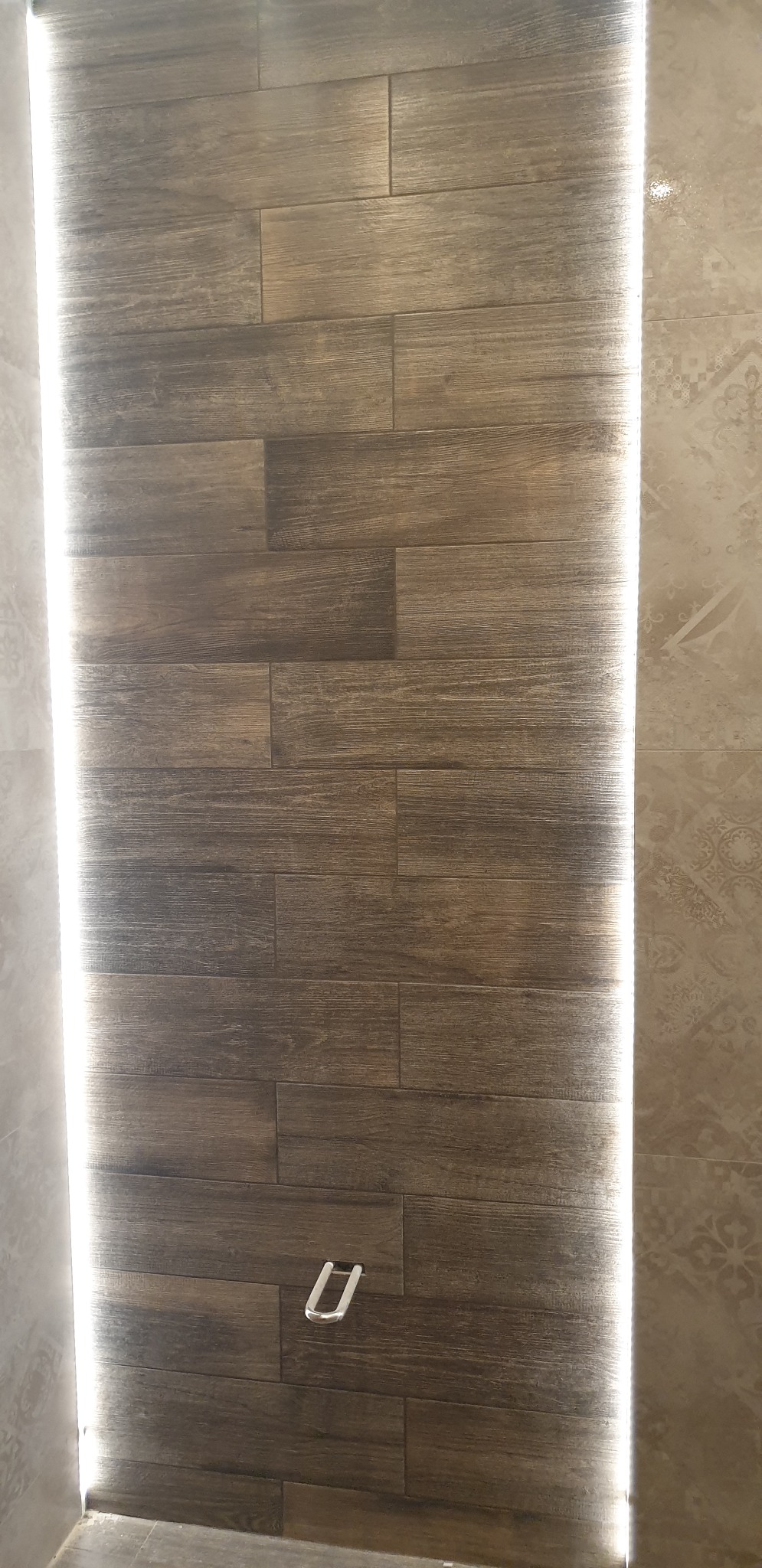 Panel ścienny imitujący drewno z oświetleniem LED po bokach i metalowym uchwytem na ręczniki w kształcie litery U.