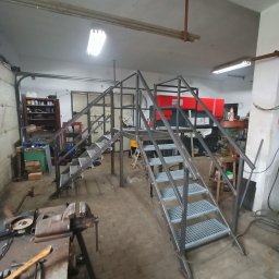 Hard Stal - Konstrukcja metalowa schodów z kratowymi stopniami, w trakcie montażu w warsztacie, widoczny stół ślusarski z imadłem i narzędziami.