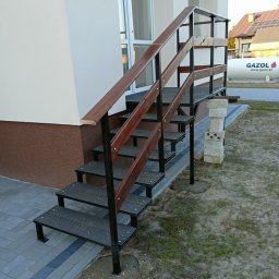 Hard Stal - Zewnętrzne schody metalowe z drewnianymi poręczami, prowadzące do drzwi wejściowych budynku, z widoczną instalacją gazową w tle.