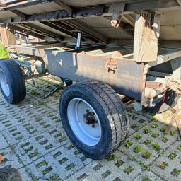 Hard Stal - Fragment przyczepy z widocznymi spawami, metalowymi elementami konstrukcyjnymi i kołami na betonowej nawierzchni z wyrastającą trawą, ukazujący realizację prac spawalniczych i konstrukcyjnych.