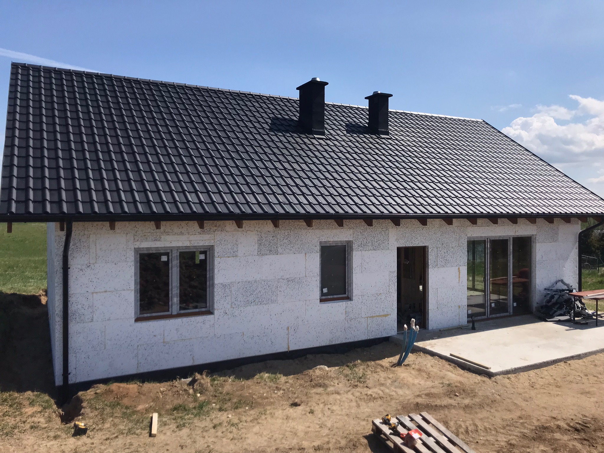 Nowy, czarny dach z dwoma kominami na surowym domu w trakcie budowy, widoczne białe ściany z pustaków.