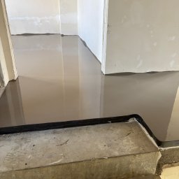 MW PODŁOGI MICHAŁ WOJCIECHOWSKI - Wylewka samopoziomująca na schodach i podłodze, przygotowana do dalszych prac wykończeniowych. Widoczne łączenie z progiem i surowe ściany.