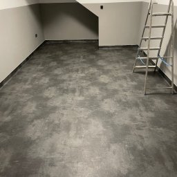 MW PODŁOGI MICHAŁ WOJCIECHOWSKI - Szara, matowa podłoga z wykładziny w pomieszczeniu z drabinką. Wykończenie ścian w dwóch odcieniach szarości, z ciemniejszym pasem na dole. Minimalistyczny design.