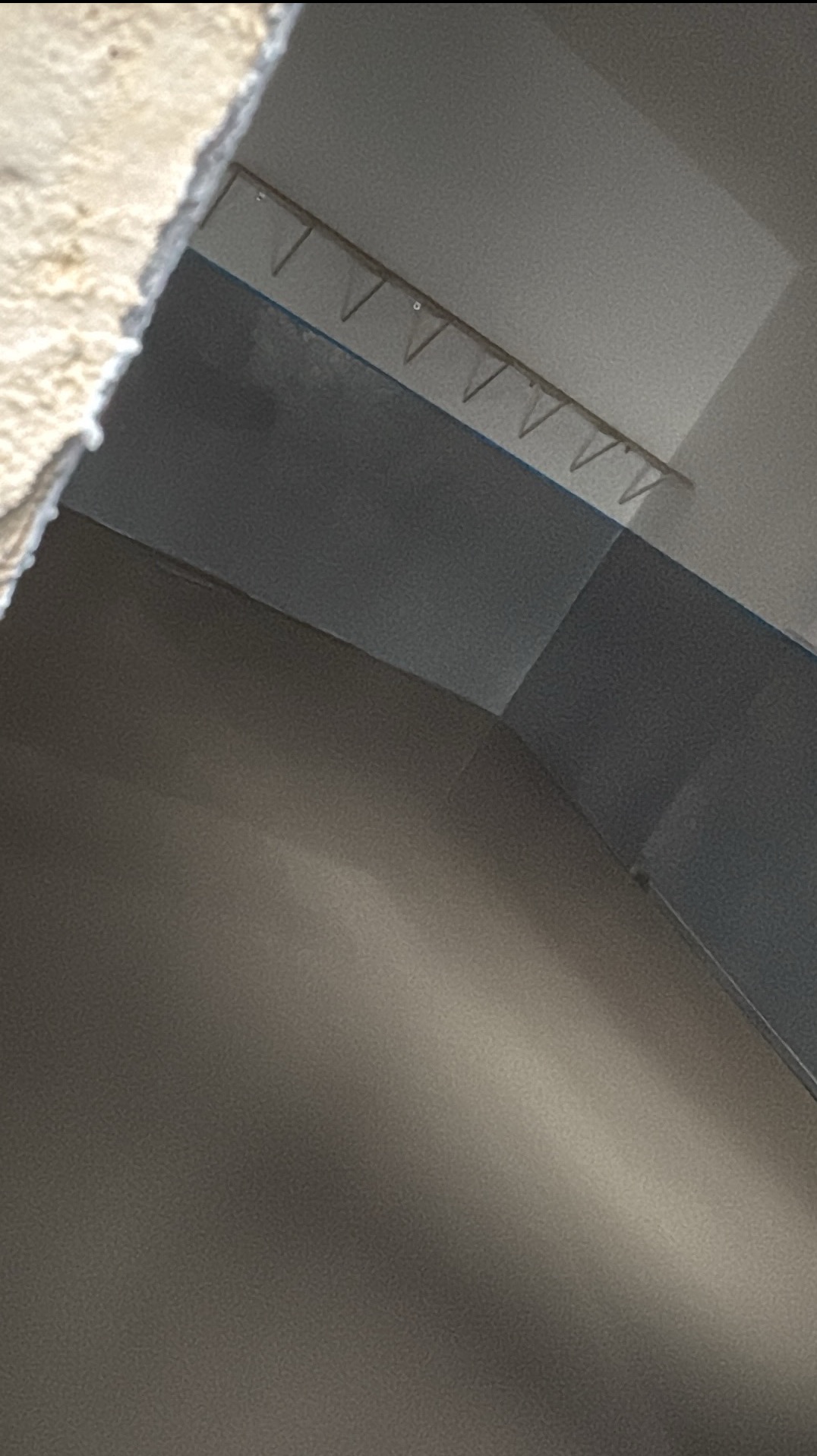 Szara wykładzina dywanowa z listwą przypodłogową i haczykami na ścianie, ujęcie z dołu, widok na róg pomieszczenia.