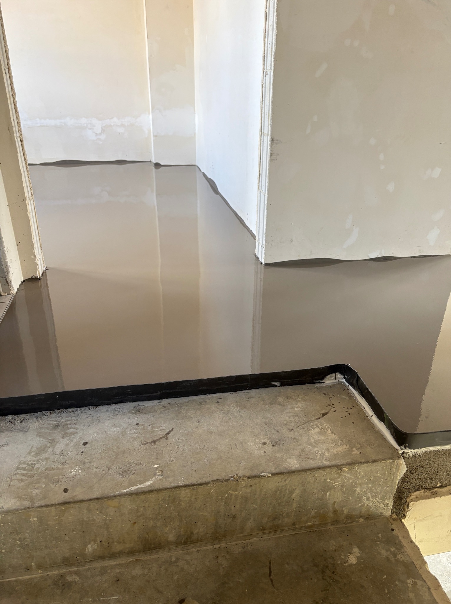 Wylewka samopoziomująca na schodach i podłodze, przygotowana do dalszych prac wykończeniowych. Widoczne łączenie z progiem i surowe ściany.