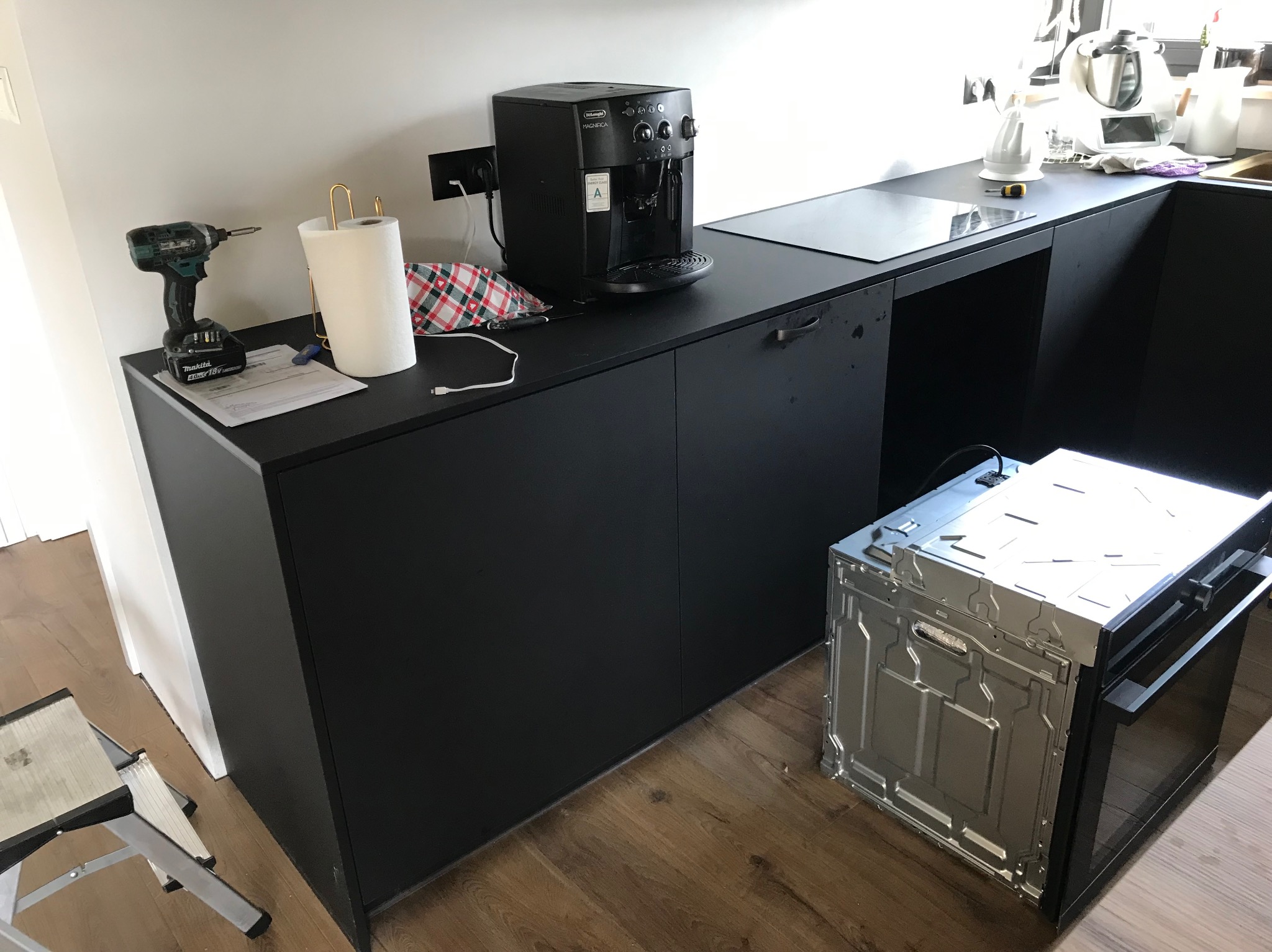 Czarna kuchnia na wymiar w trakcie montażu: widoczna wnęka na piekarnik, ekspres do kawy i narzędzia na blacie. Ustawienie frontem do kamery, oświetlenie dzienne.