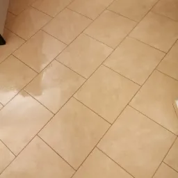 Ułożona pod kątem beżowa podłoga z płytek ceramicznych, widoczne fugi i częściowo fragment szafki.