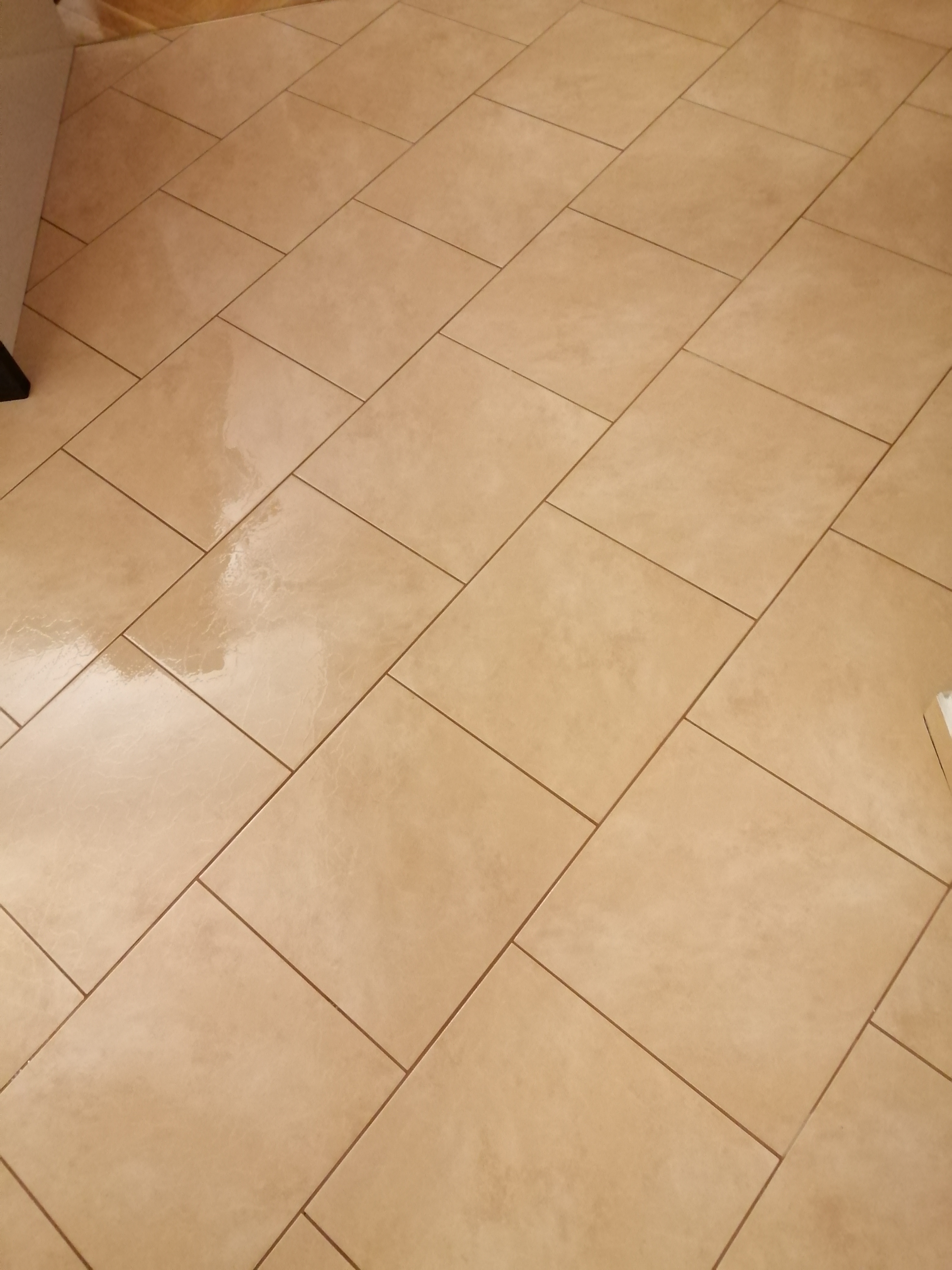 Ułożona pod kątem beżowa podłoga z płytek ceramicznych, widoczne fugi i częściowo fragment szafki.