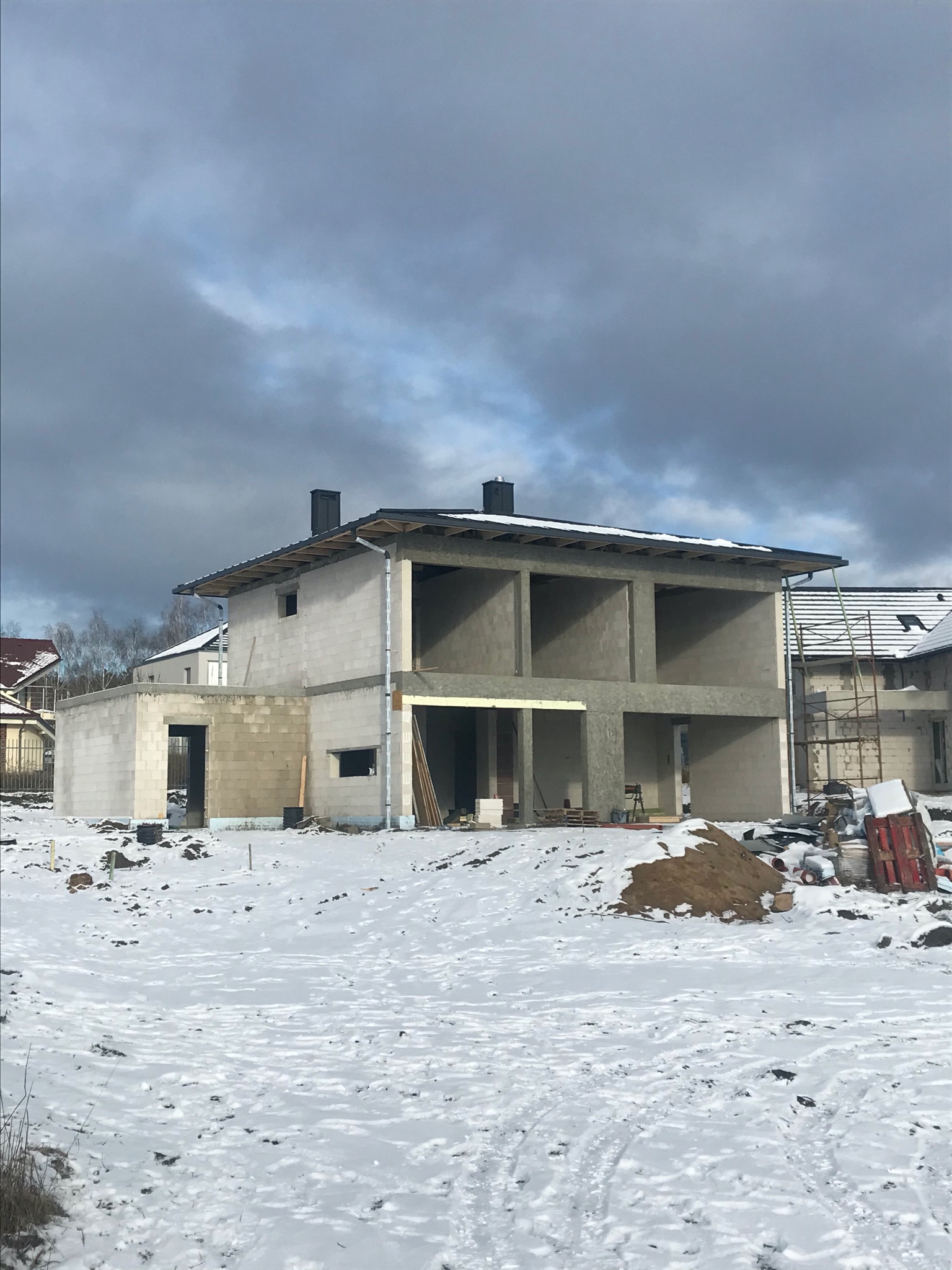 Surowy stan dwukondygnacyjnego budynku z betonu komórkowego w zimowej scenerii, widoczne otwory okienne i drzwiowe bez stolarki, na pierwszym planie śnieg.