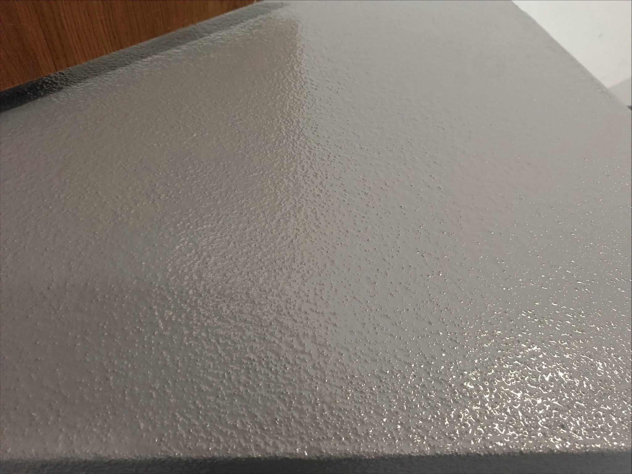 Zbliżenie szarej, chropowatej powierzchni, prawdopodobnie posadzki, w kolorze RAL 7040 z widoczną strukturą i refleksami światła.