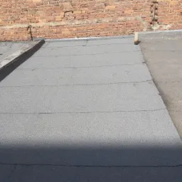 Płaski dach pokryty papą termozgrzewalną, widoczna ceglana ściana budynku i metalowe obróbki blacharskie.