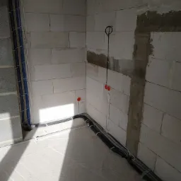 Surowy stan: Kable elektryczne ułożone w peszlach i przymocowane do ściany z betonu komórkowego, widoczne puszki instalacyjne i przewody pionowe, fragment ściany z naprawionym ubytkiem.