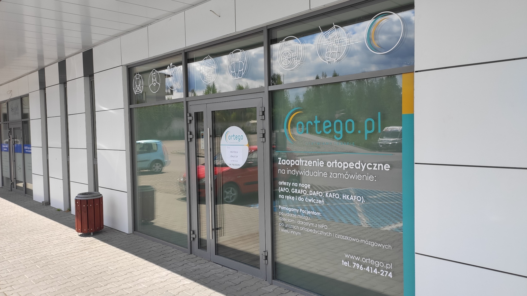 Oklejona witryna firmy ortopedycznej Cortego.pl z informacjami o zaopatrzeniu ortopedycznym i numerem telefonu, ozdobiona grafikami ortez.