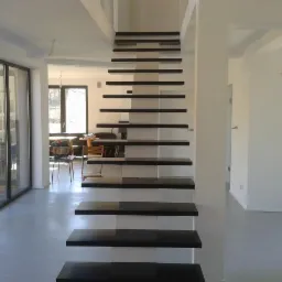 Nowoczesne schody wspornikowe z ciemnego drewna w minimalistycznym wnętrzu z dużymi oknami i szarą podłogą.