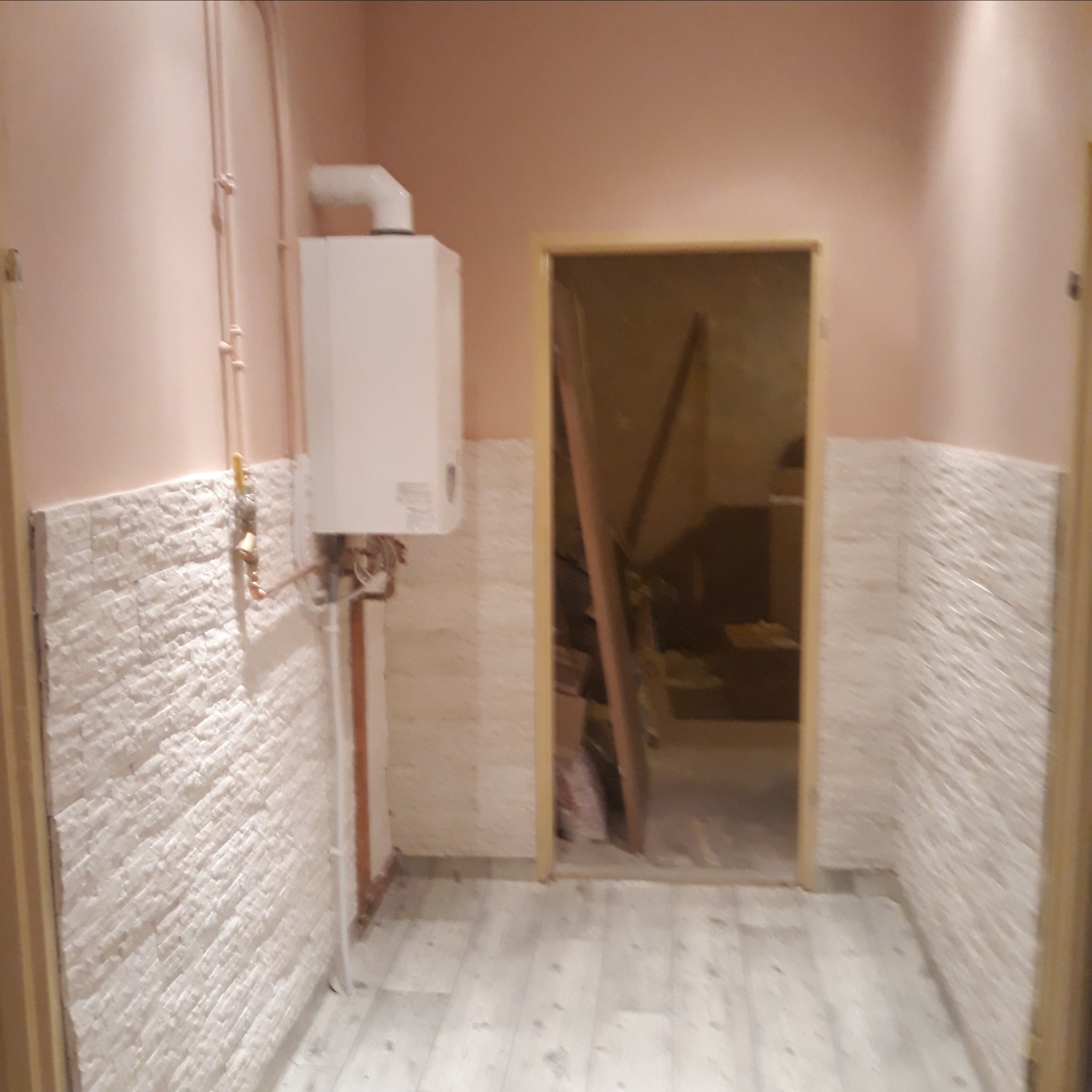 Wnętrze w Zapałowie w trakcie prac wykończeniowych: ściany wyłożone dekoracyjną płytką imitującą kamień, widoczny piec gazowy i przygotowane wejście do pomieszczenia.