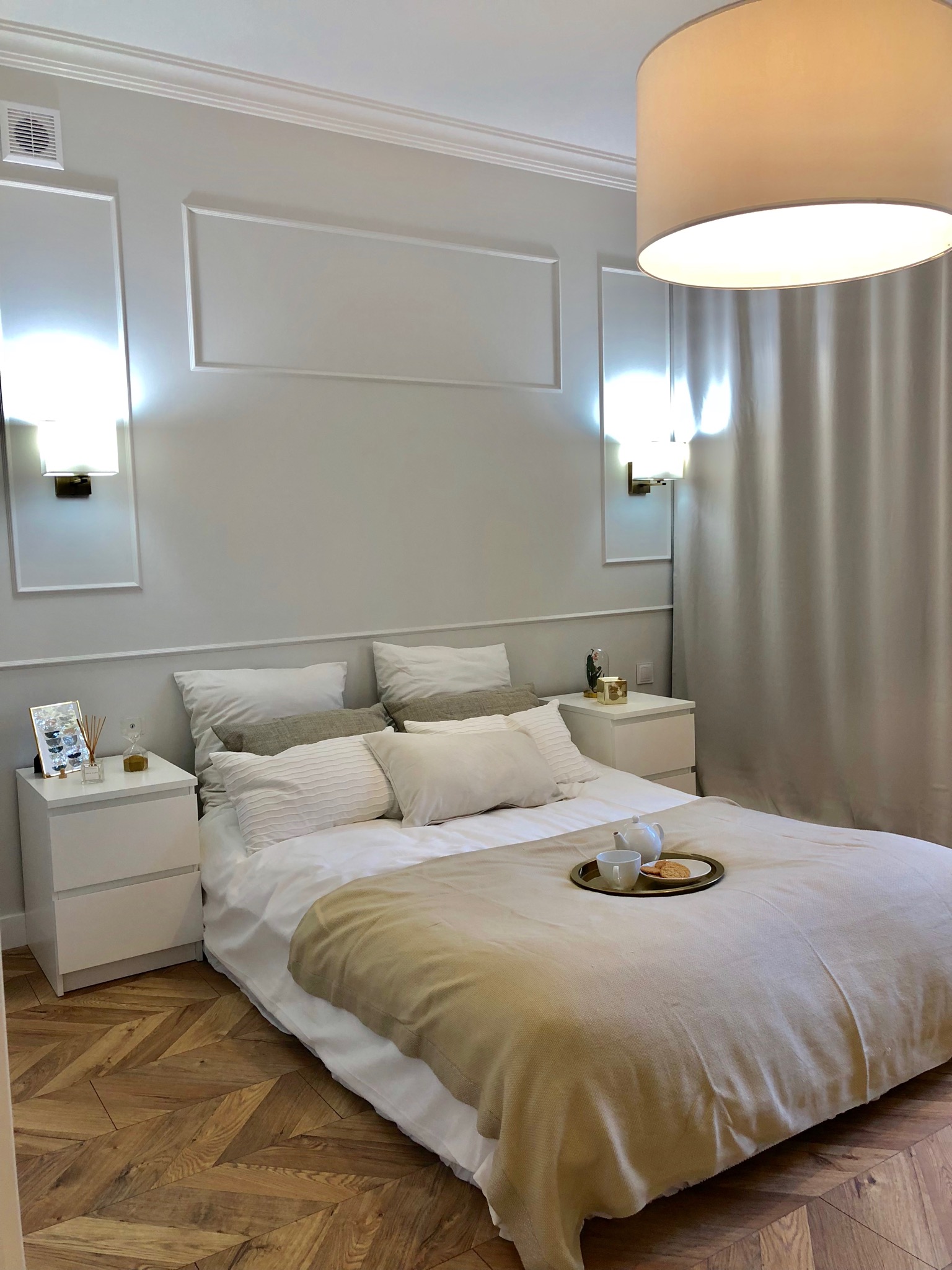 Elegancka sypialnia w jasnych barwach z parkietem w jodełkę, dekoracyjnymi panelami ściennymi i śniadaniem na łóżku.