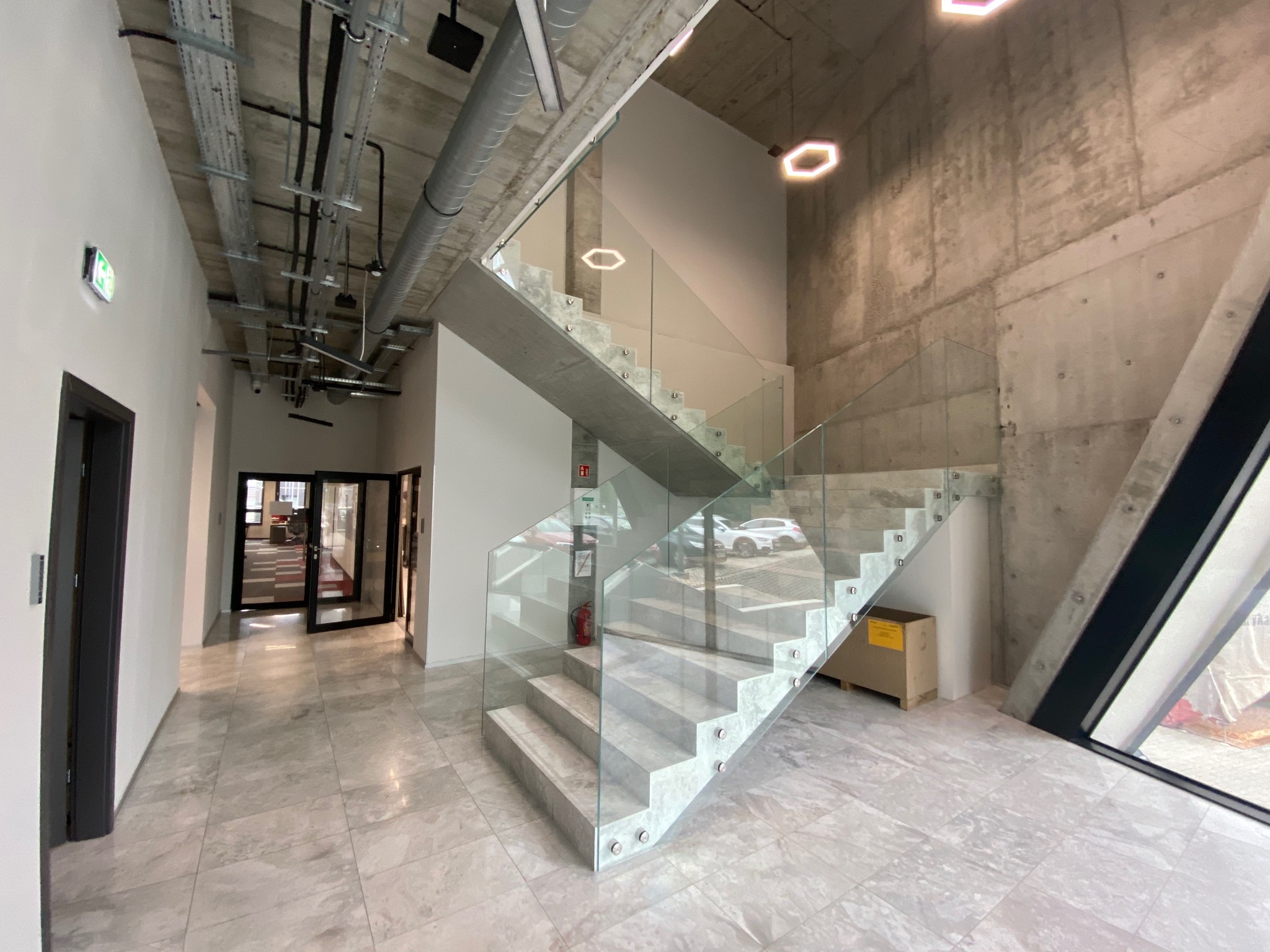 Nowoczesne schody z betonu i szkła w Chorzowie, widoczne instalacje pod sufitem i marmurowa podłoga.