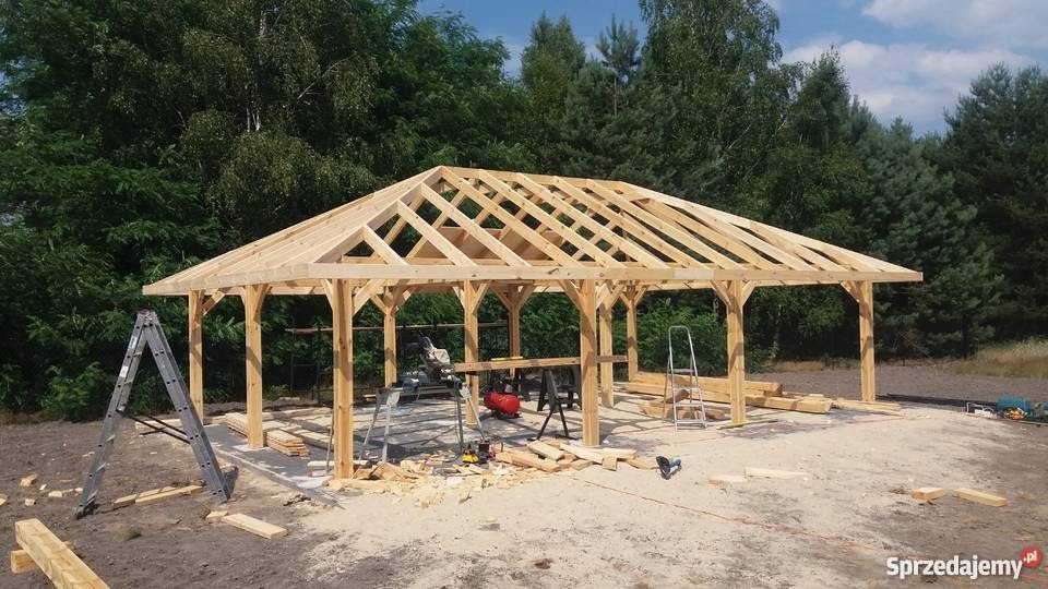 Drewniana konstrukcja zadaszenia w trakcie budowy w Złotoryi, widoczne narzędzia, drabiny i częściowo ułożona więźba dachowa na tle zieleni.