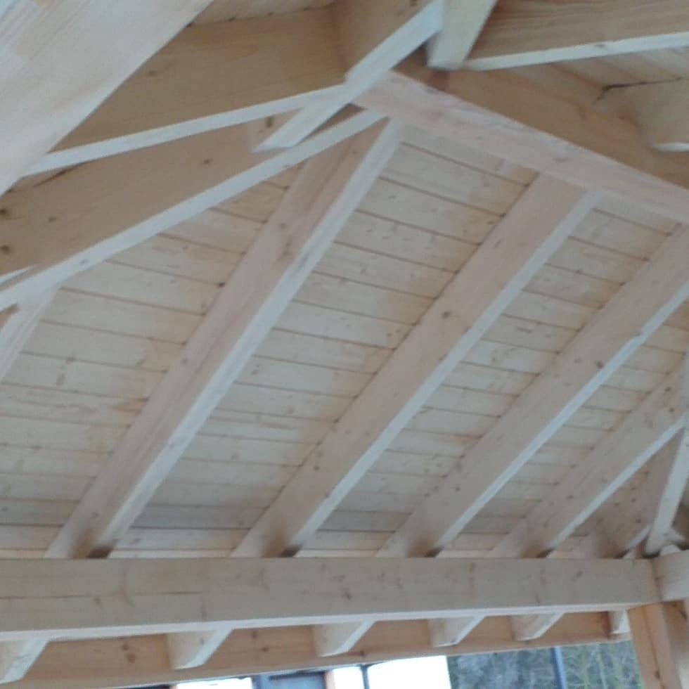 Surowa drewniana konstrukcja dachu z widocznymi belkami i deskami, jasne drewno, widok od wewnątrz.