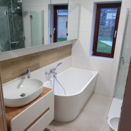 Welus - Nowoczesna łazienka z białymi płytkami, drewnopodobnym akcentem nad umywalką, owalną wanną i oknem z widokiem na zewnątrz.