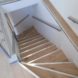 Wewnętrzne drewniane schody z metalowymi wykończeniami stopni i metalową balustradą, prowadzące w dół do piwnicy lub innego pomieszczenia.