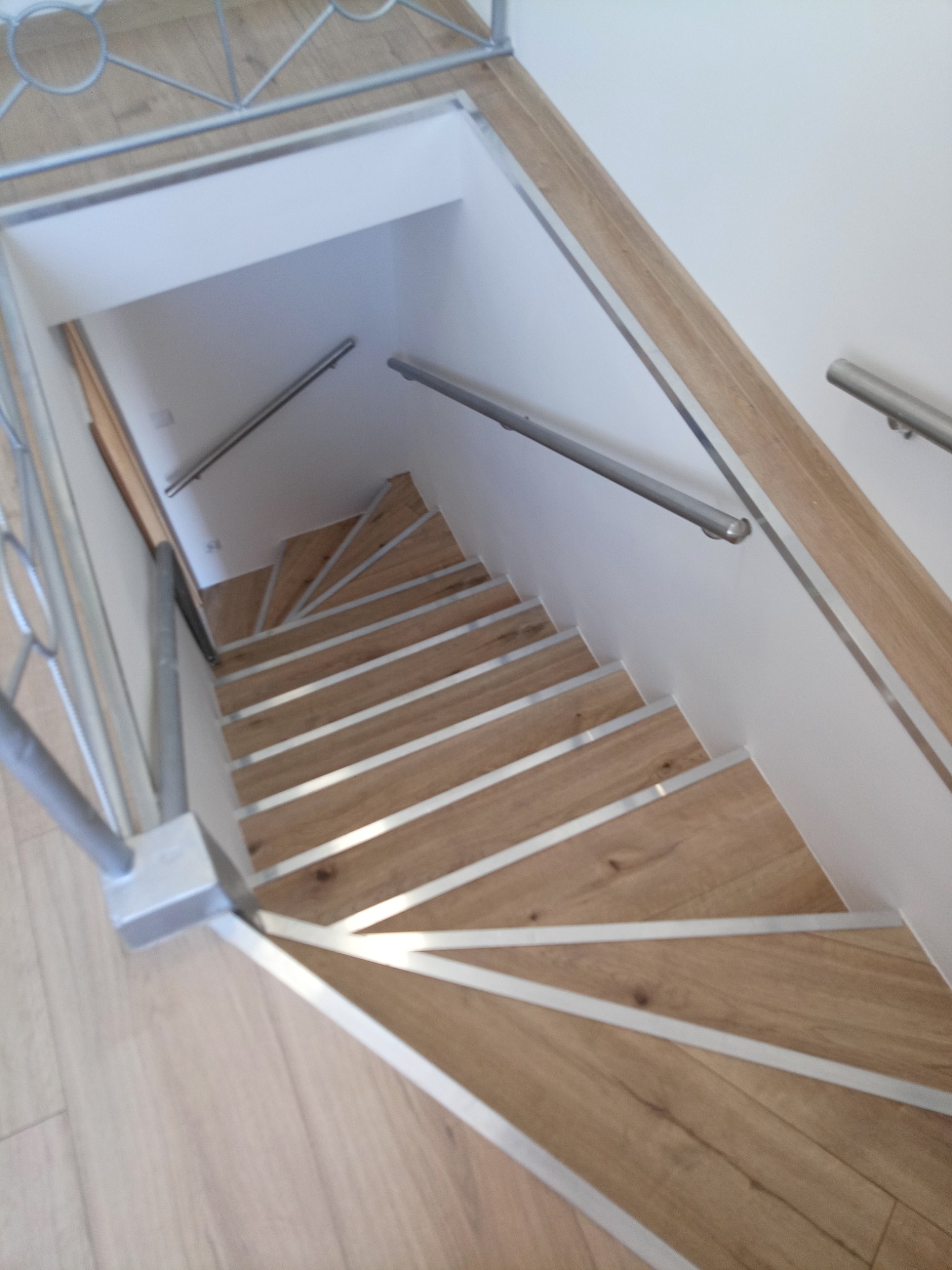 Wewnętrzne drewniane schody z metalowymi wykończeniami stopni i metalową balustradą, prowadzące w dół do piwnicy lub innego pomieszczenia.