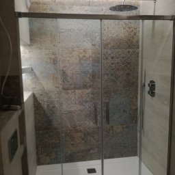 DECOTEL Mariusz Dudek - Kabina prysznicowa z przesuwnymi drzwiami, wykończona płytkami w odcieniach beżu i brązu z delikatnym wzorem, widoczna deszczownica i bateria termostatyczna.