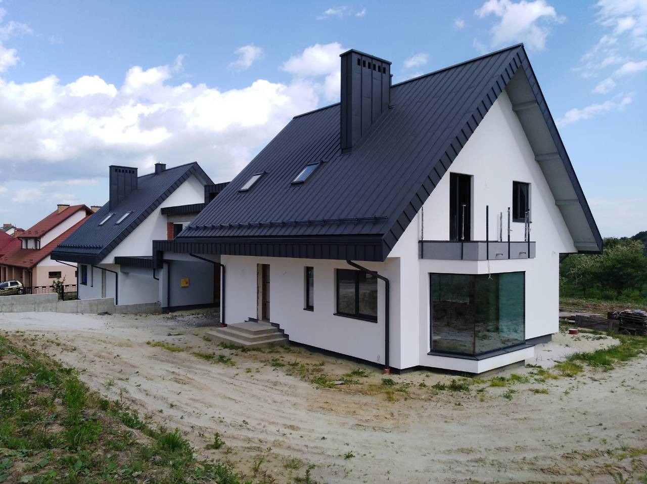 Nowoczesny dom jednorodzinny z czarnym dachem i białymi ścianami, widoczny z zewnątrz, na etapie wykończenia terenu.