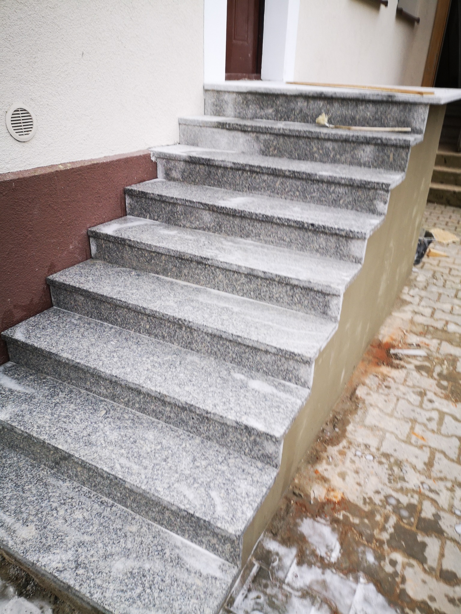 Granitowe schody zewnętrzne w trakcie montażu, widoczne świeże zaprawy i niedokończone obrzeże, ceglana podłoga częściowo zabrudzona.