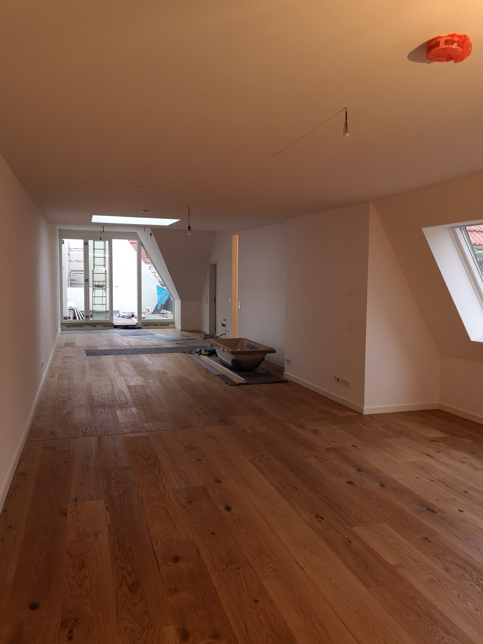 Przestronne wnętrze w trakcie prac wykończeniowych: świeżo położony parkiet, przygotowana do montażu wanna na zabezpieczonej podłodze, widoczne wyprowadzenia instalacji elektrycznej na suficie...