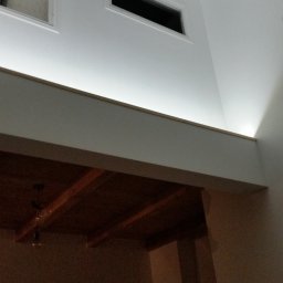 Baufirma Orczykowski - Wysoki pokój z antresolą, widoczne okna w dachu i na górnej ścianie, oświetlenie LED pod antresolą, drewniany sufit antresoli.