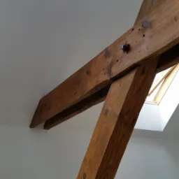 Drewniana konstrukcja więźby dachowej z widocznym oknem dachowym i gładkimi, pomalowanymi na biało ścianami.