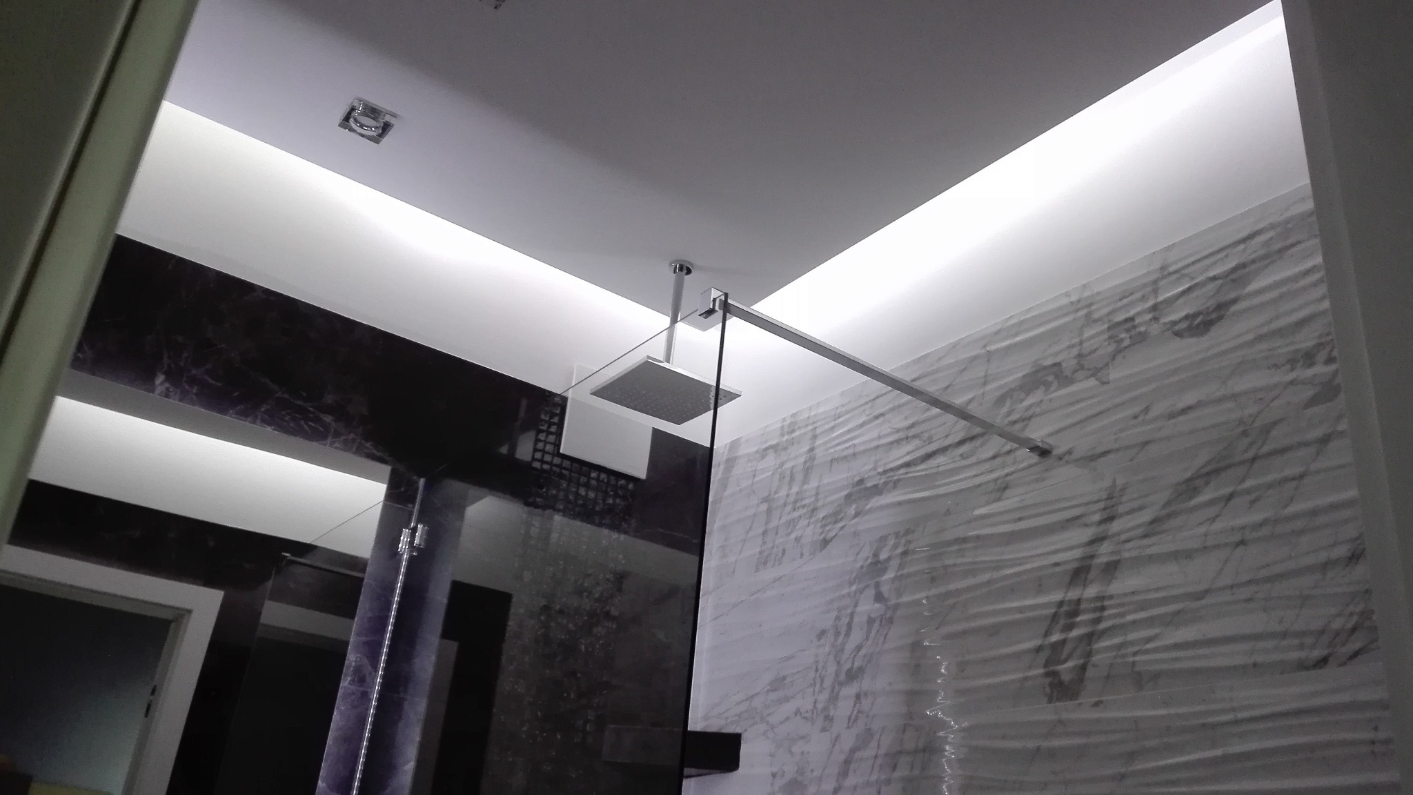 Nowoczesna łazienka z kabiną prysznicową typu walk-in, marmurowymi płytkami na ścianie i podświetlanym sufitem podwieszanym.