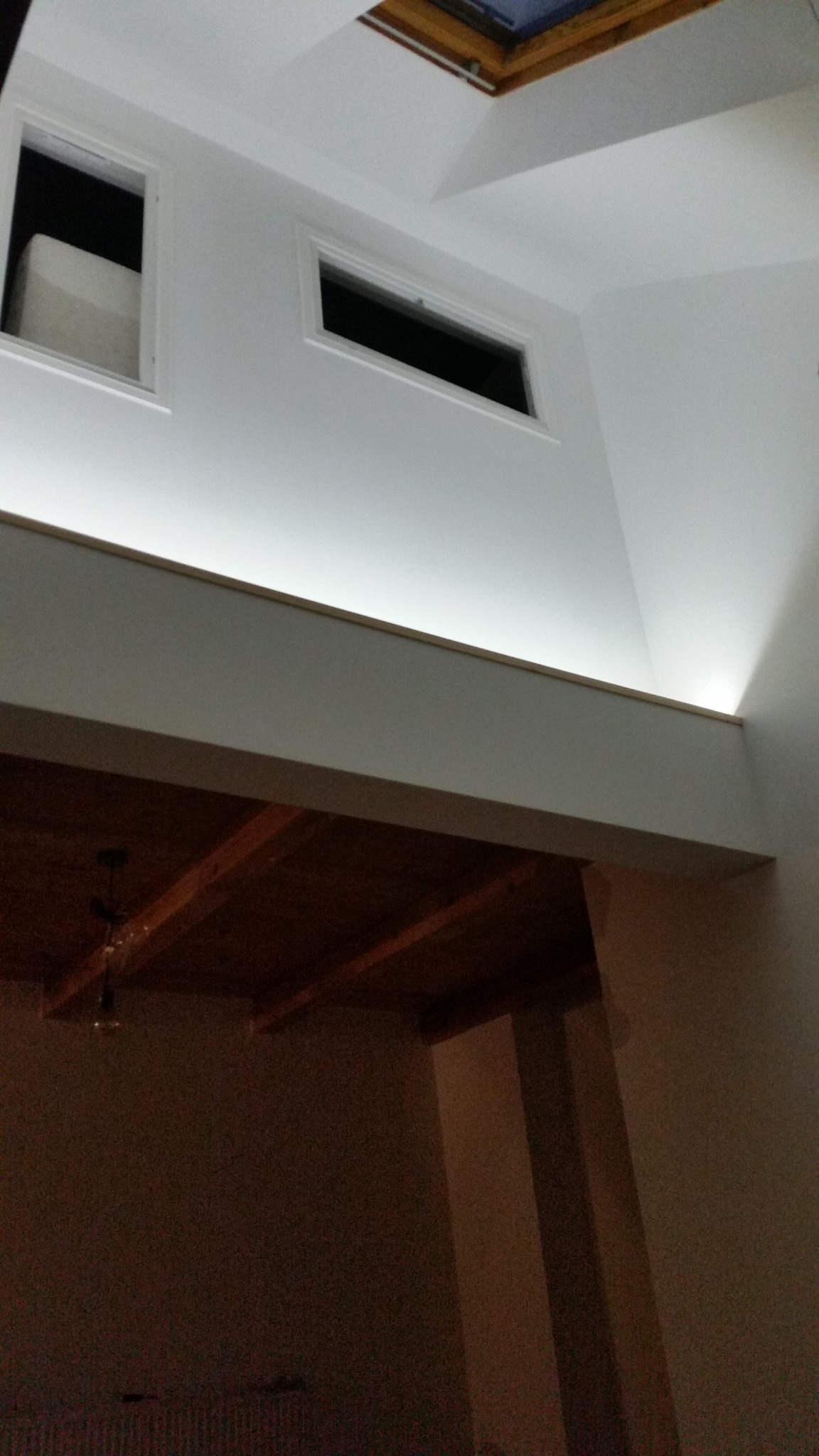 Wysoki pokój z antresolą, widoczne okna w dachu i na górnej ścianie, oświetlenie LED pod antresolą, drewniany sufit antresoli.