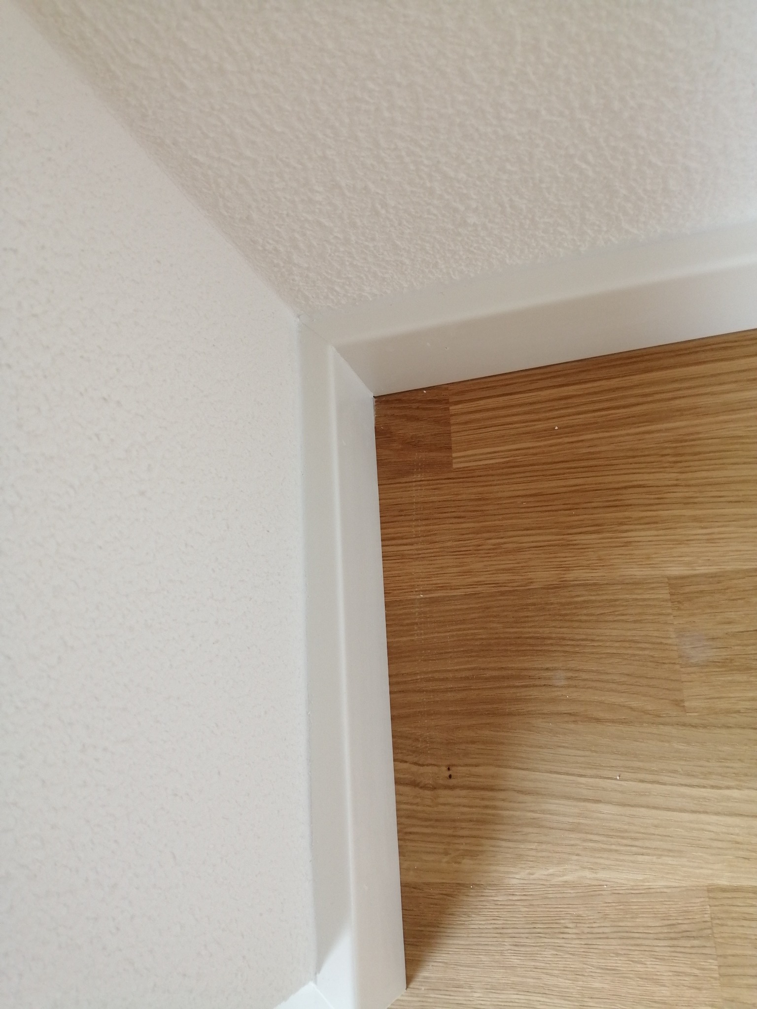 Fragment wnętrza po remoncie: jasny parkiet, białe listwy przypodłogowe i ściana o delikatnej strukturze, z widocznym narożnikiem pokoju.