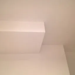 Fragment białego sufitu z otworem na oświetlenie i obniżonym elementem, widok z dołu.