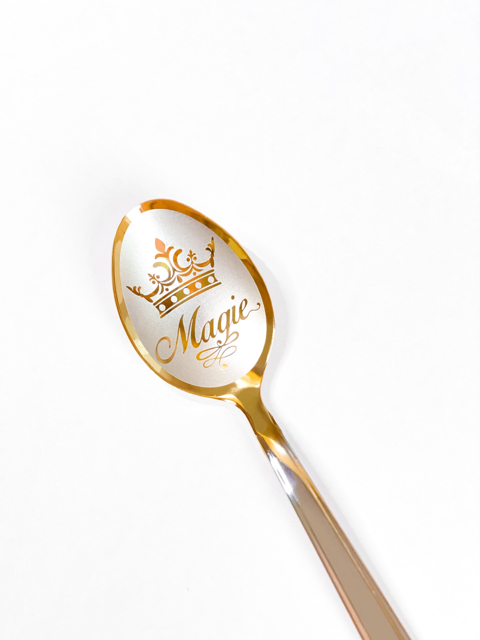 Złota łyżeczka z grawerem korony i napisem 'Magie' na białym tle.